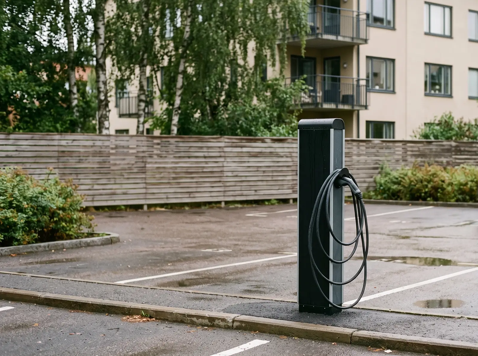Laddstolpe med upphängd laddkabel på en parkering vid ett flerbostadshus